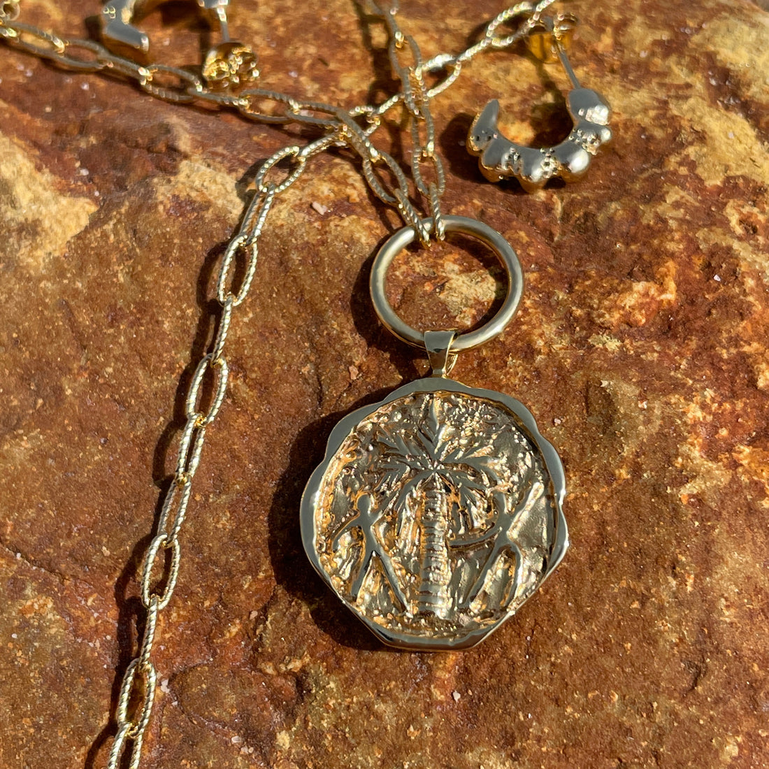 Palm dance talisman coin pendant in gold vermeil on an orange rock.