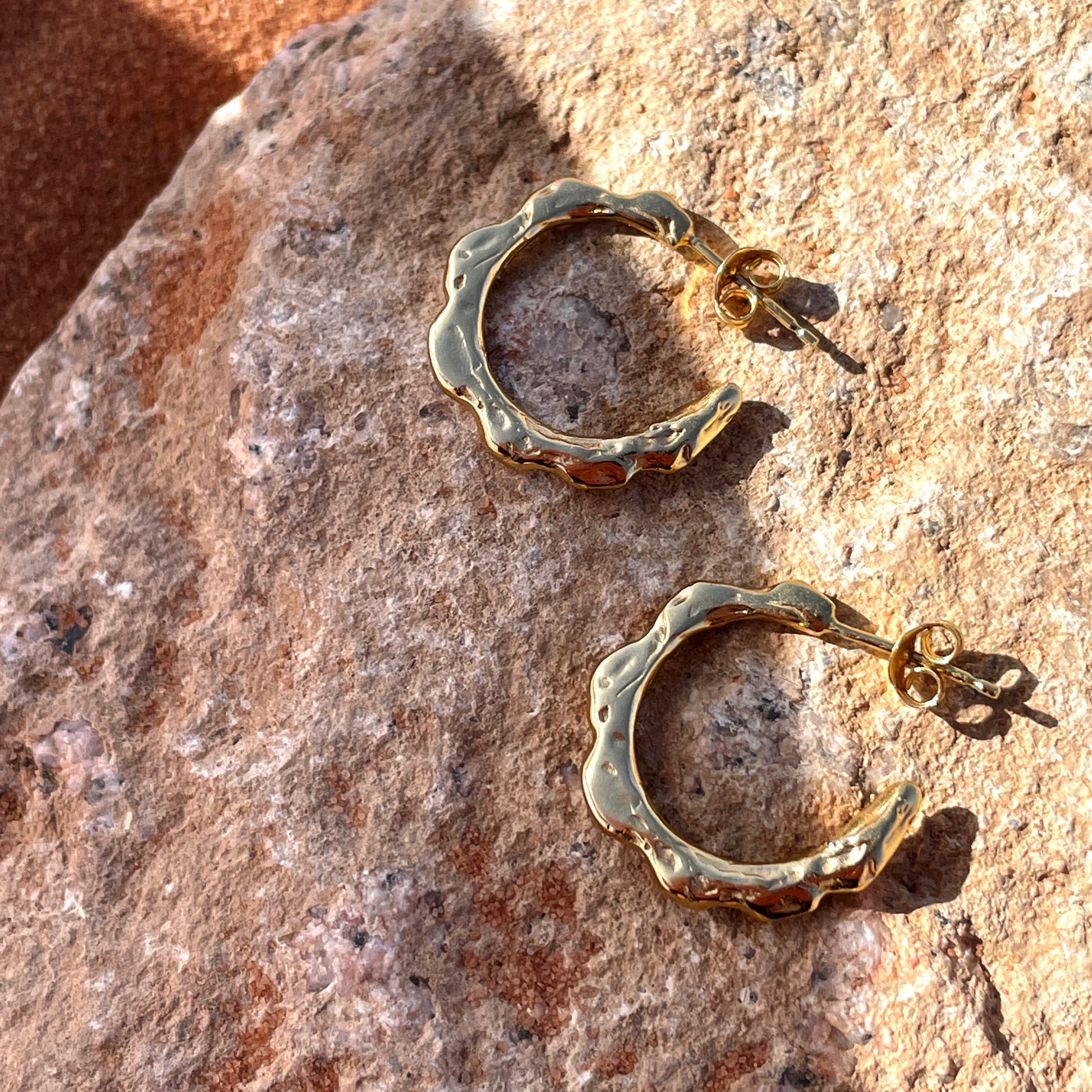 Gold hoop earrings with organic texture, laying on a rock.