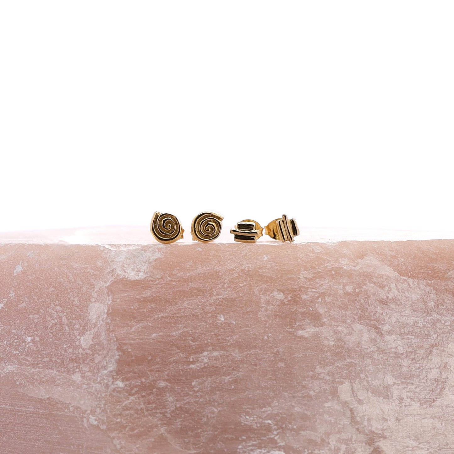 Two pairs of gold stud earrings resting on a piece of rose quartz.