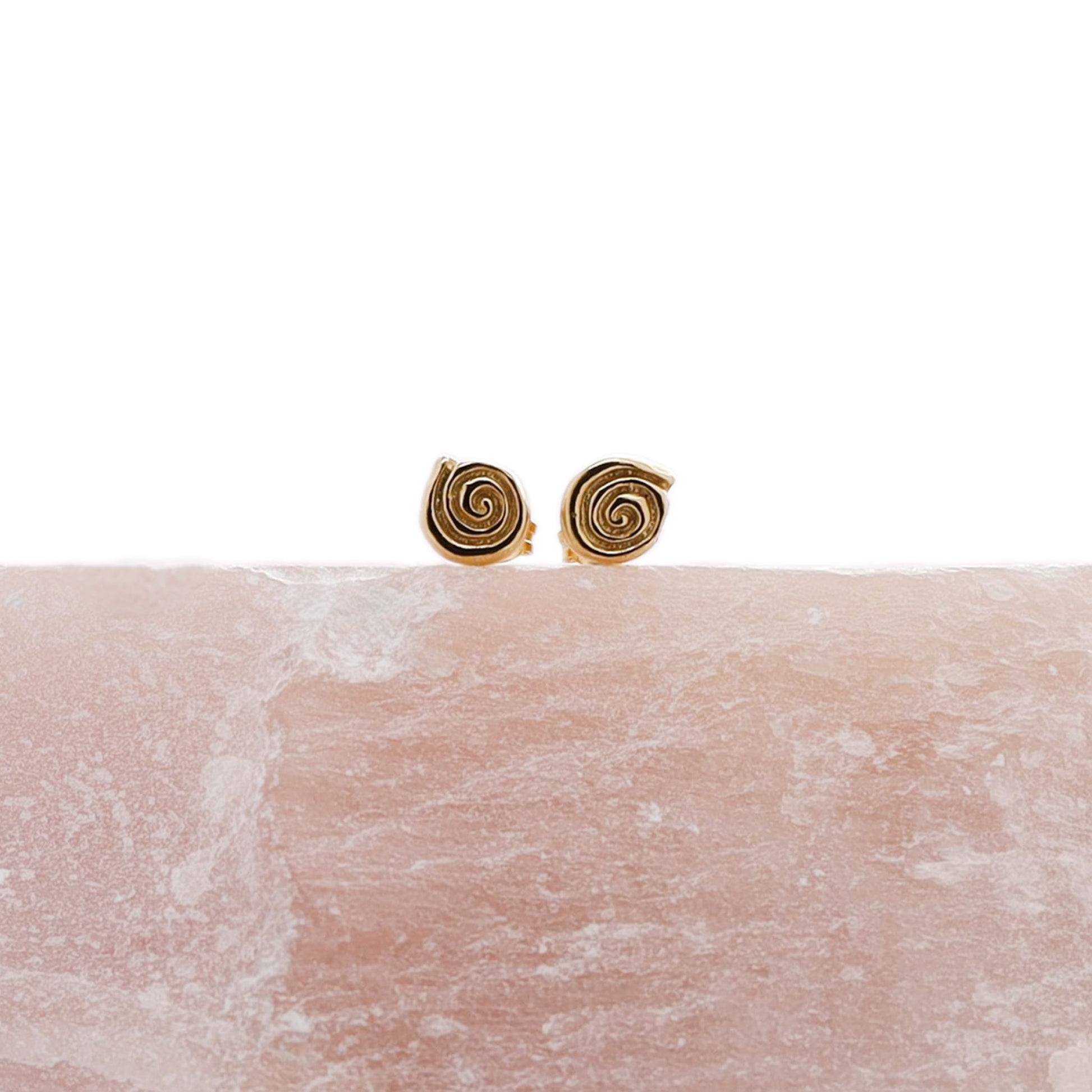 Small gold labyrinth stud earrings on a piece of rose quartz.