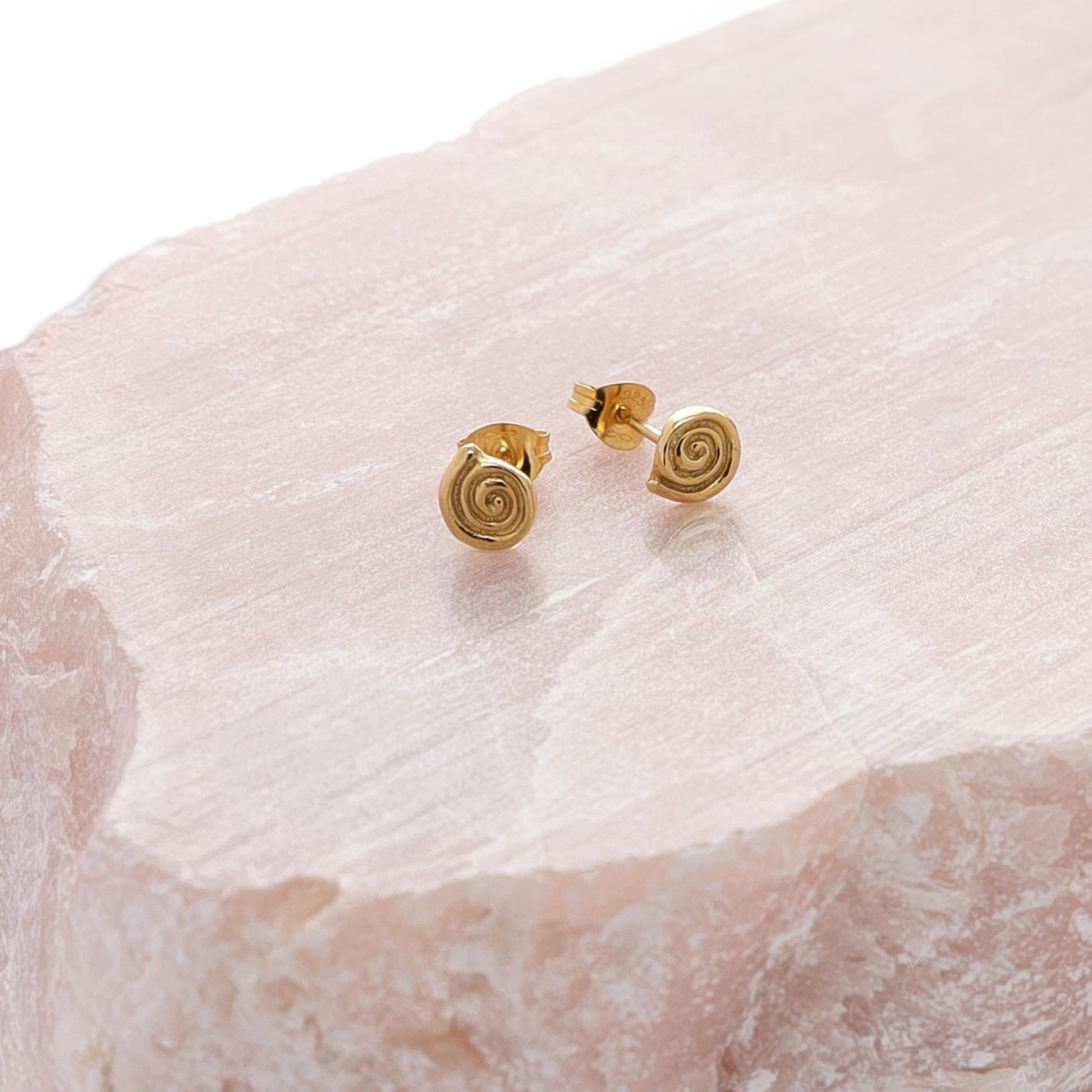 Small gold labyrinth stud earrings on a piece of rose quartz.