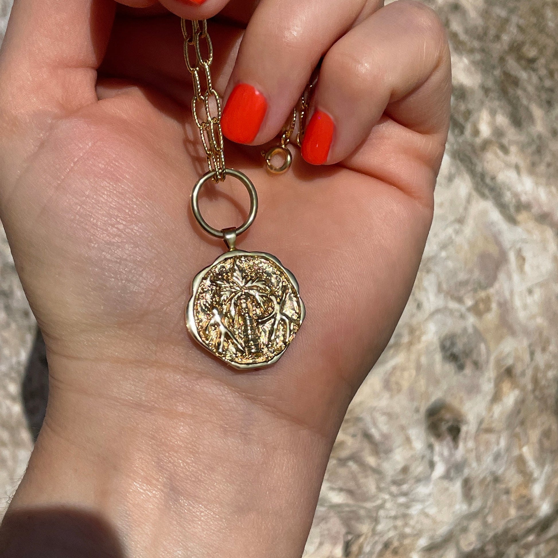 Gold coin pendant necklace engraved with a palm tree and two people dancing around it. 