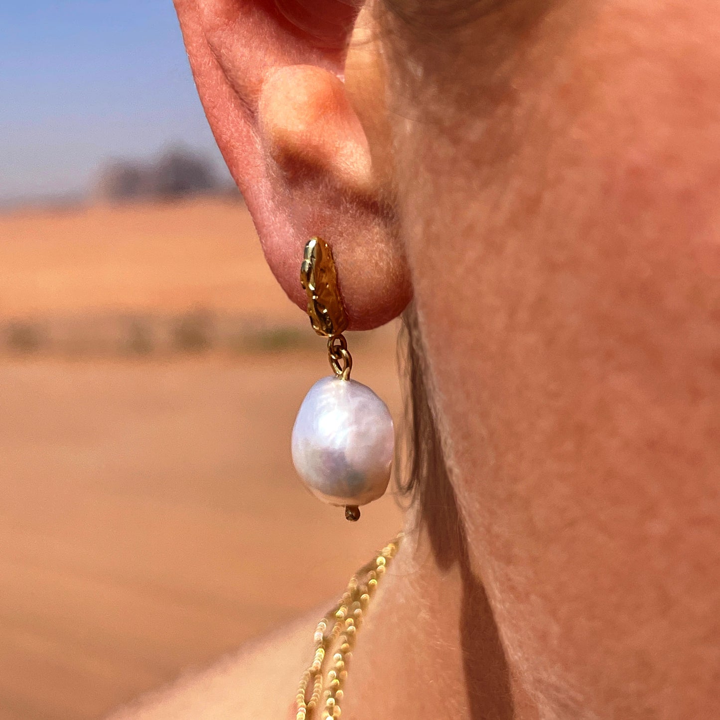 A close up of a an ear wearing a drop baroque pearl earring with a gold textured fixing.