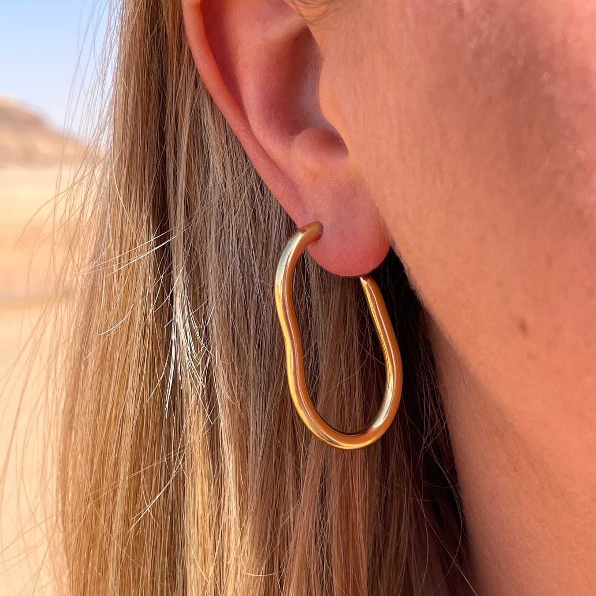 A close up of a large gold pebble shape hoop earring being worn.