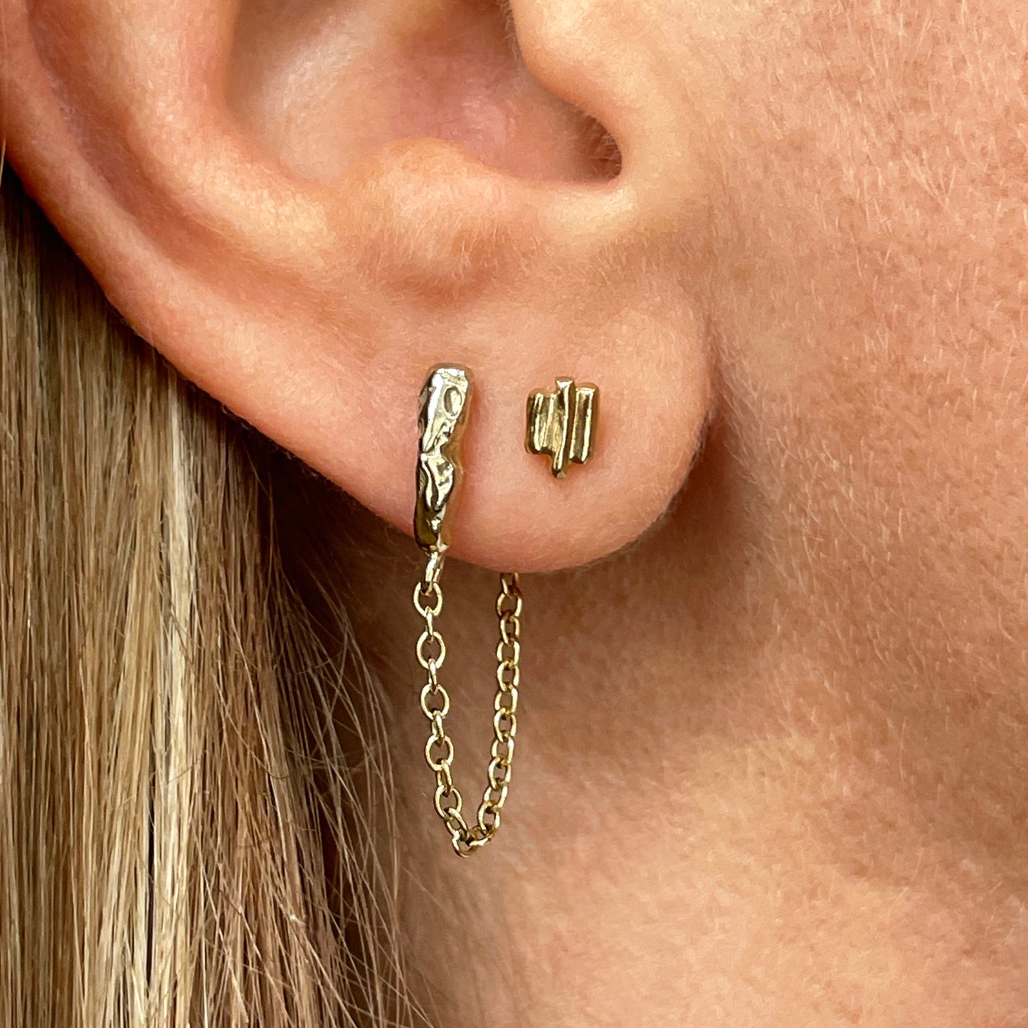 Close up of and ear with two gold stud earrings.