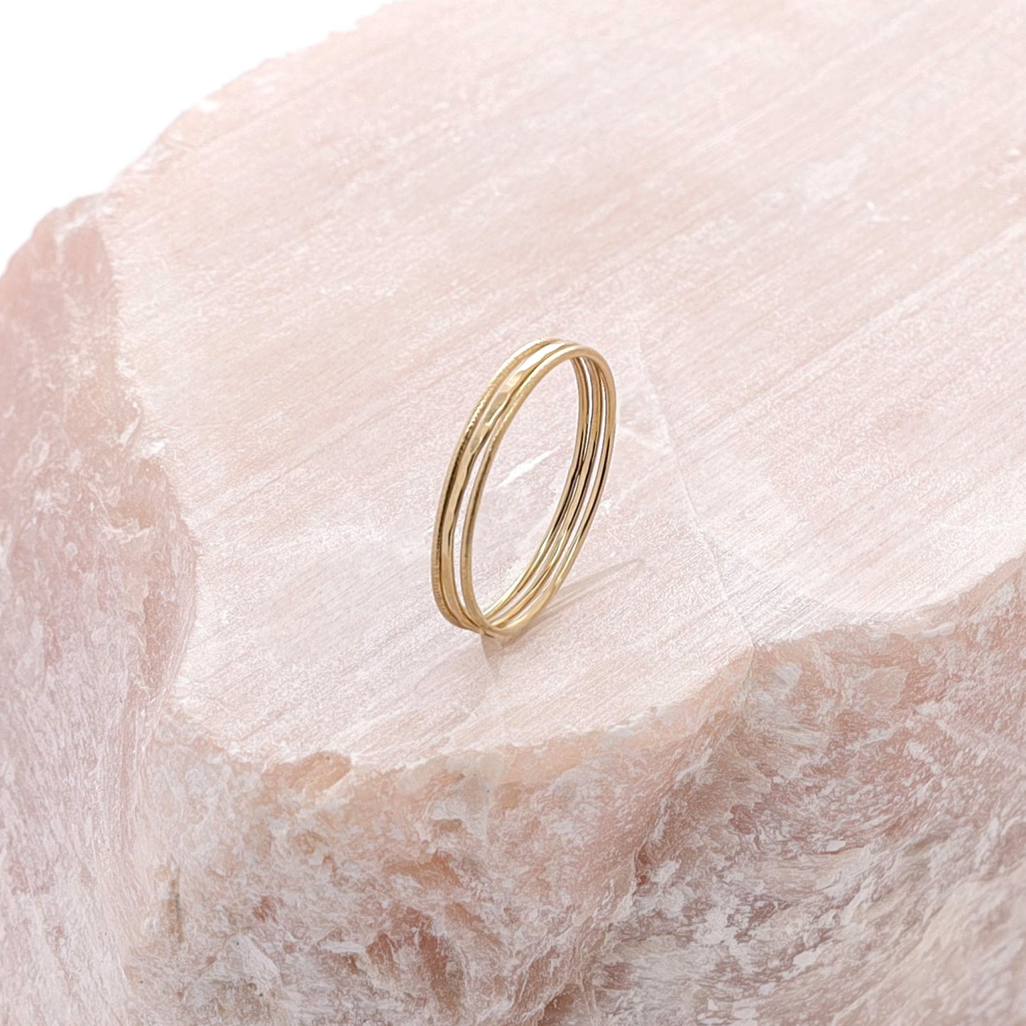 Three slim gold stacking rings, each with a different texture, displayed on a large piece of rose quartz.