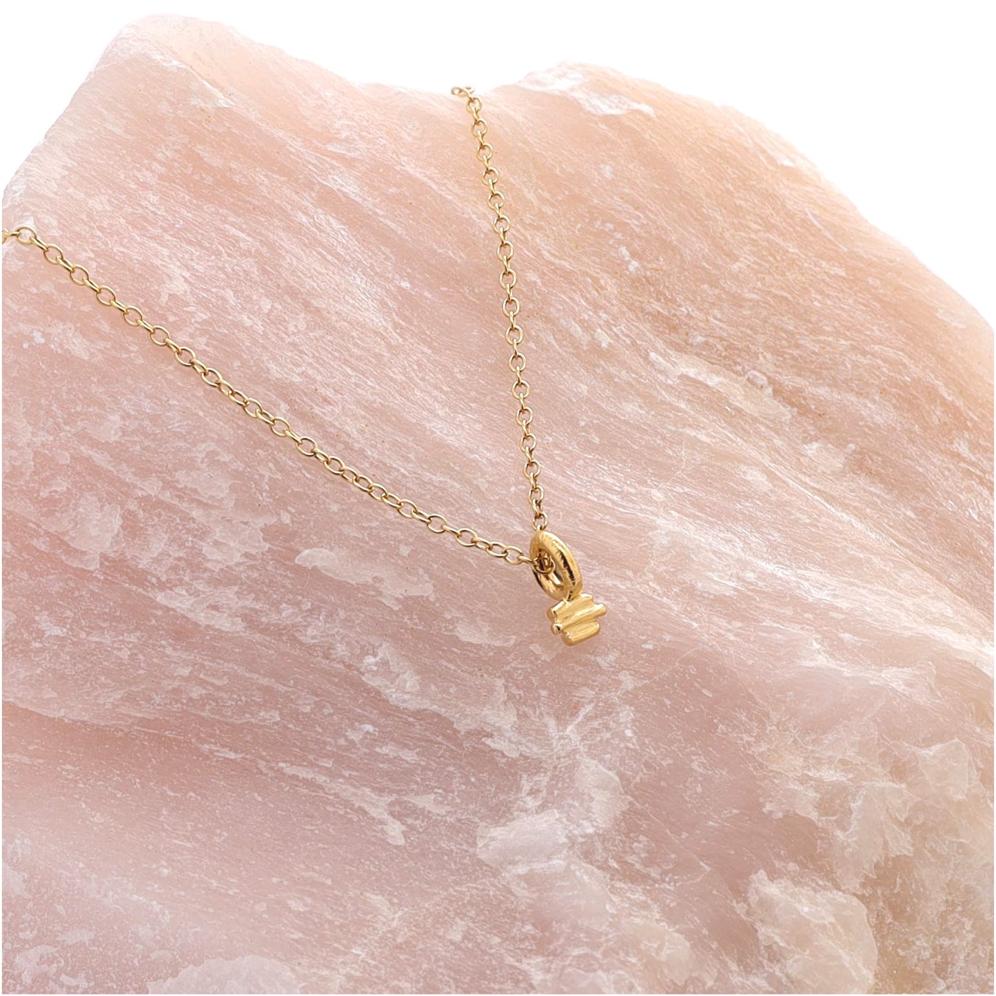 Small gold textured charm on a fine gold chain draped over a large piece of rose quartz.