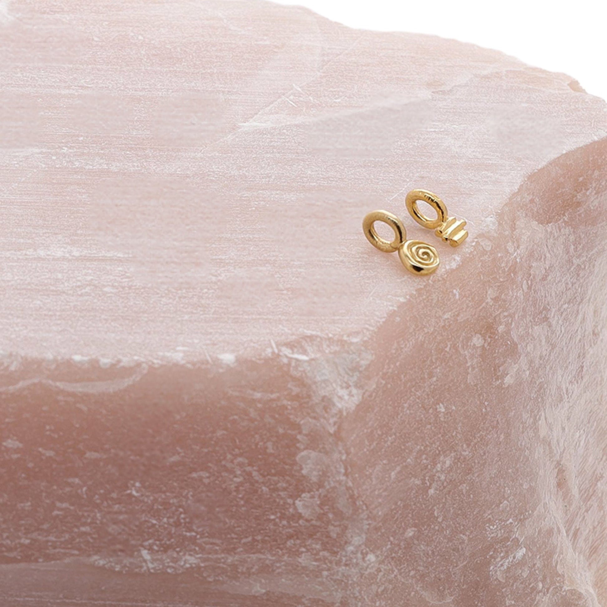 Two small gold charms sat on a piece of rose quartz.