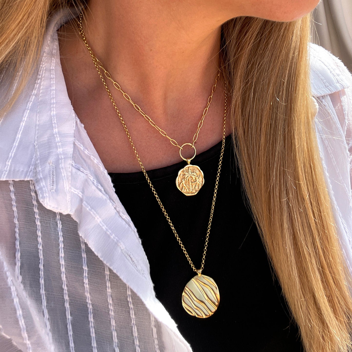 A close up of a lady with blonde hair, wearing two gold coin pendants necklaces.