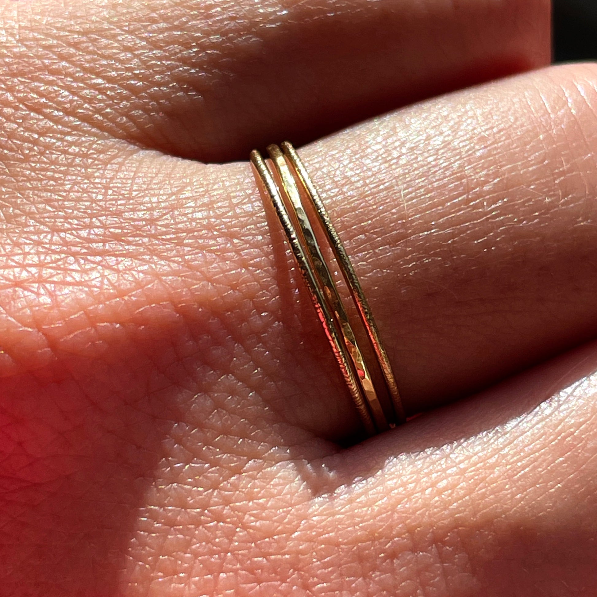 Three slim gold stacking rings, each with a different texture, being worn on the middle finger of the model.